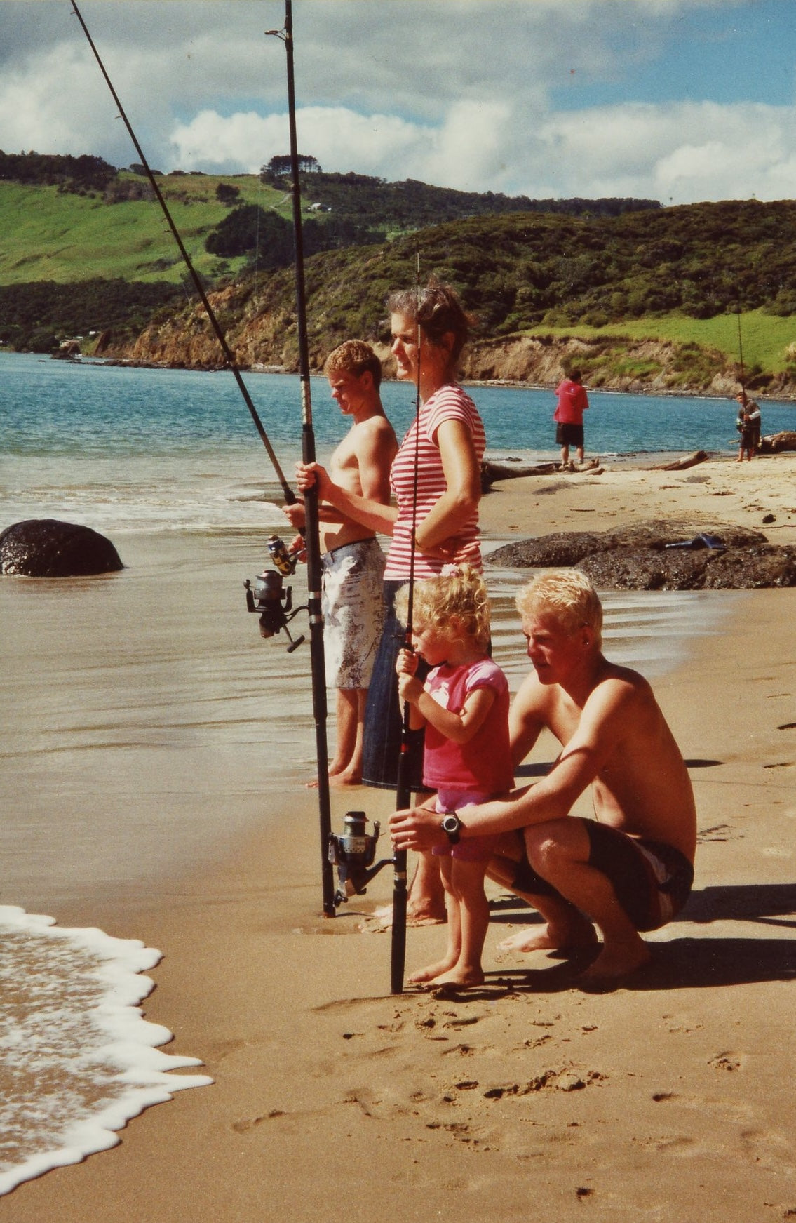 The Suckling family enjoys fishing on a sandy beach with the ocean and green hills in the background.