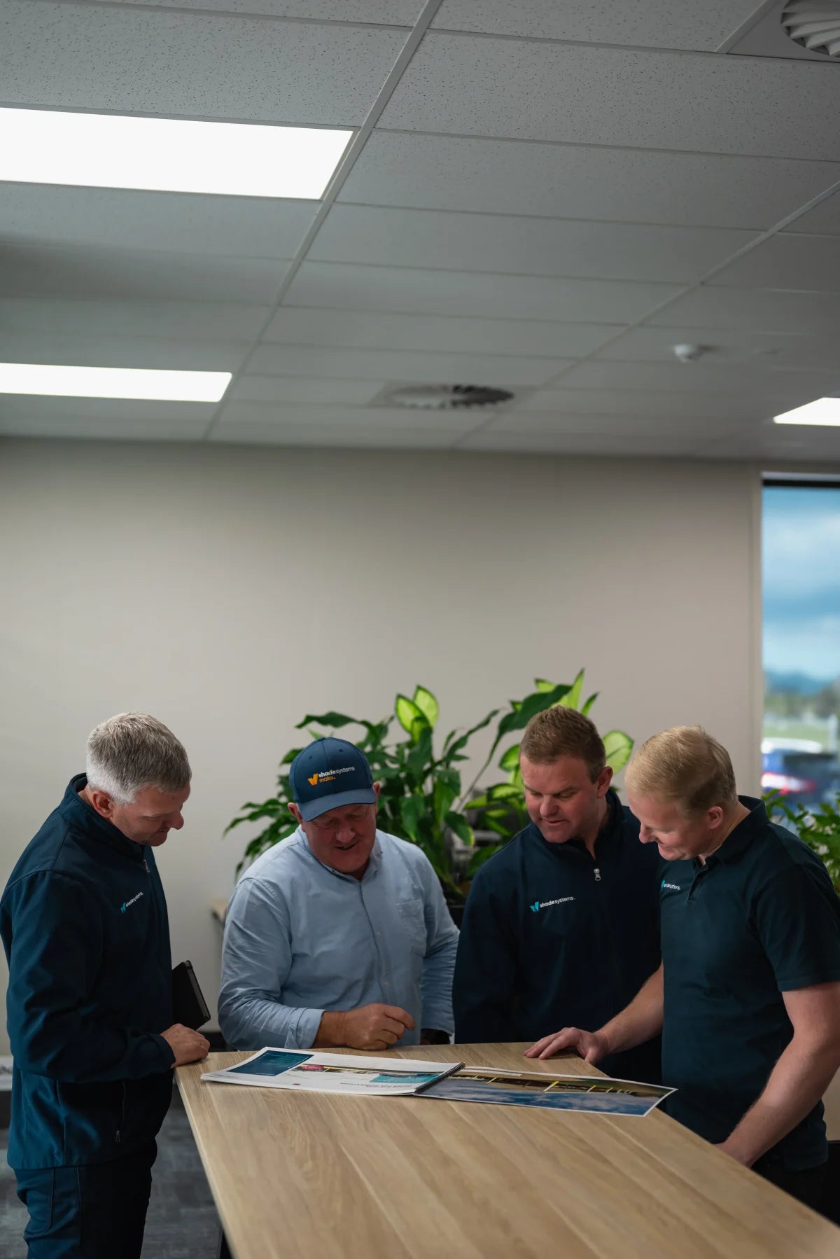 The ShadeSpace director and his three sons gathered around a light wood table in an office setting, looking at printed documents. 