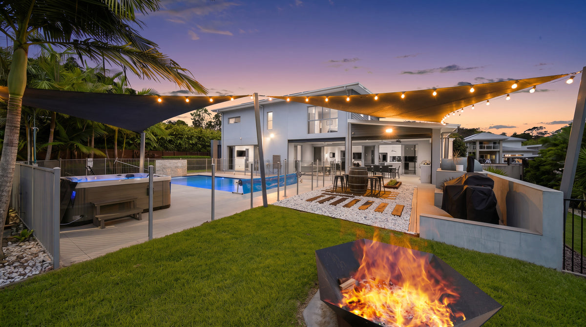 String lights attached to a shade sail with Koru Clips above a modern backyard pool and patio at dusk.